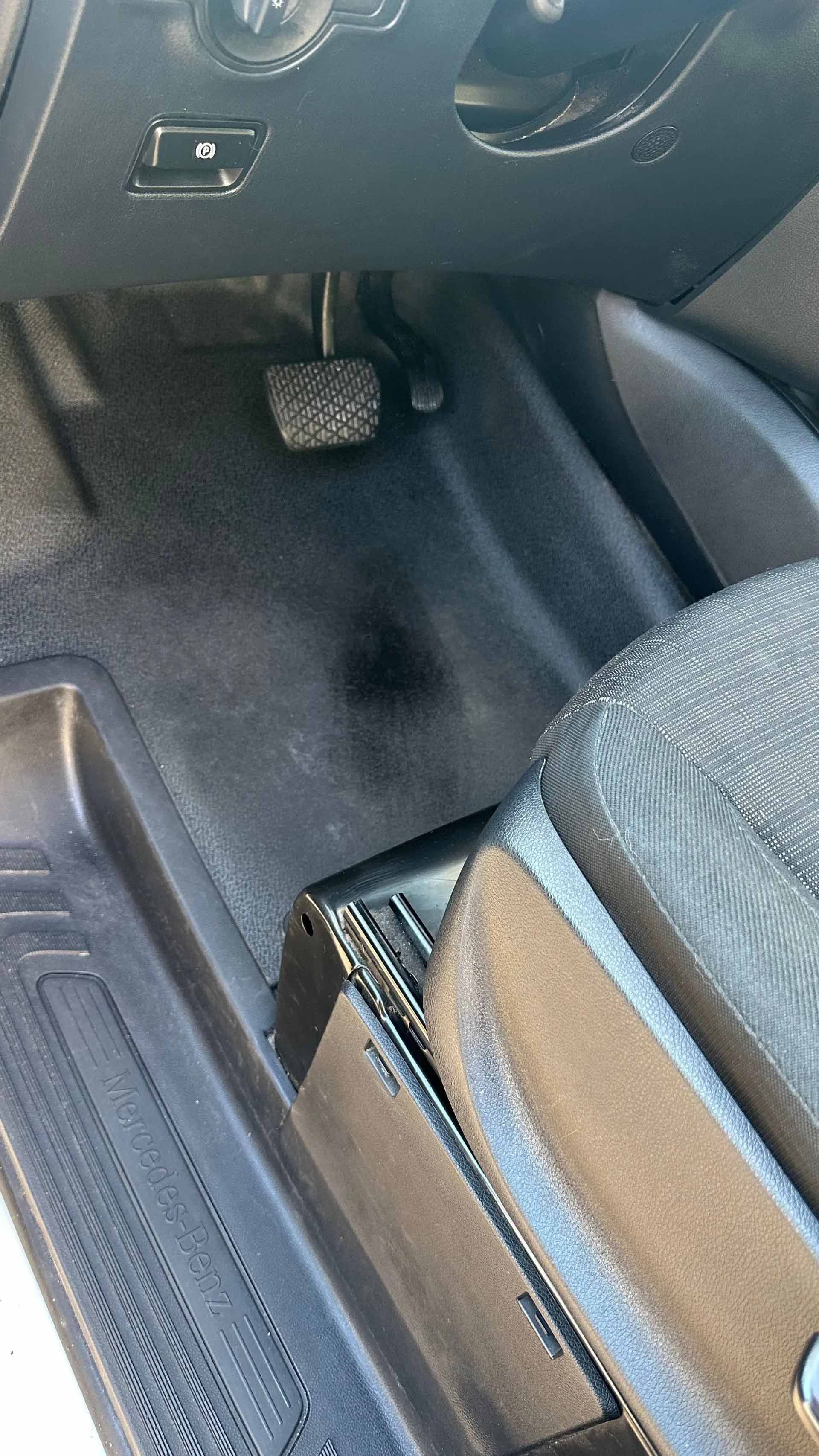 Intérieur de voiture noir avec pédales, tapis de sol et partie de siège.