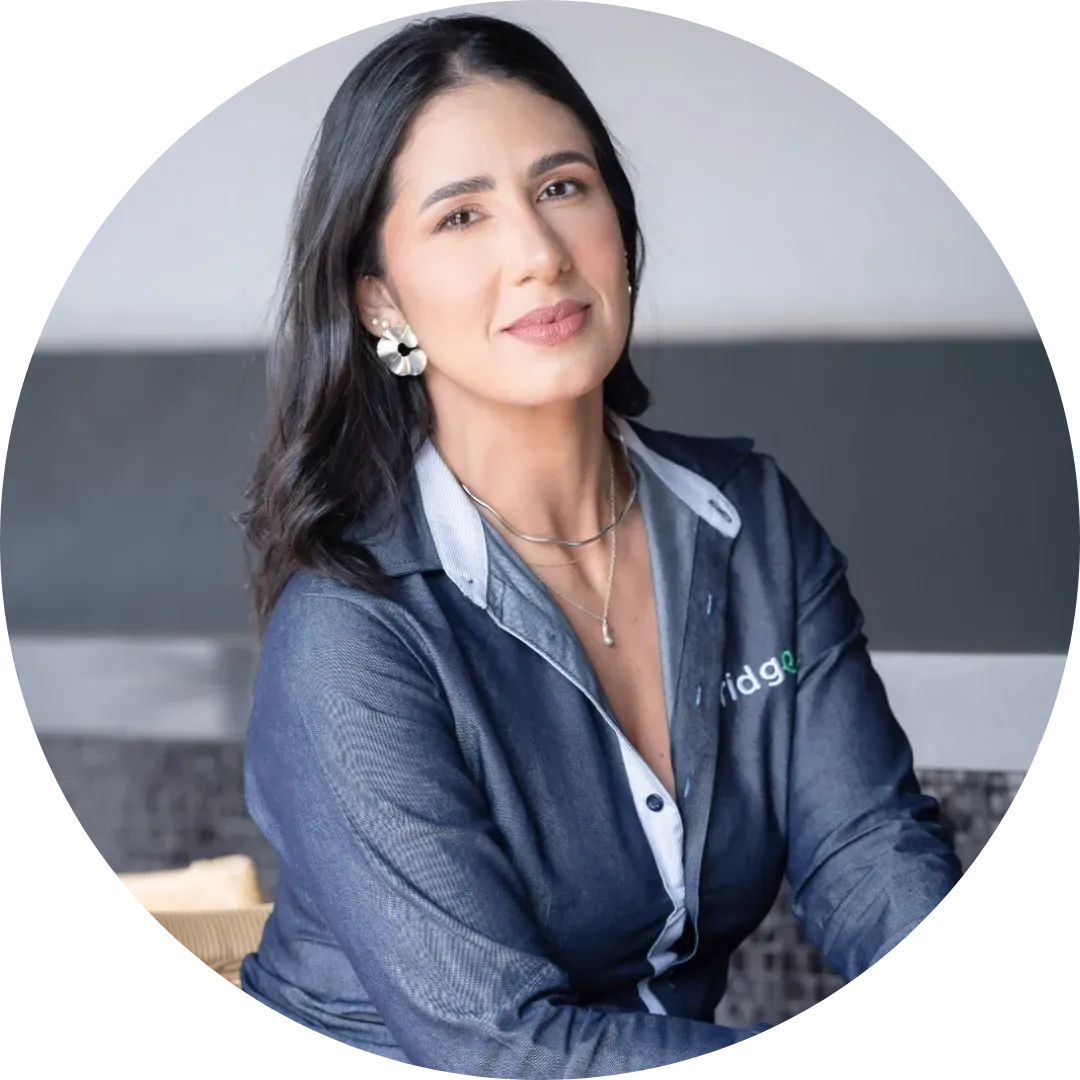 Uma mulher vestindo uma camisa azul uniforme Bridge Gestão Social e brincos está sentada em círculo.