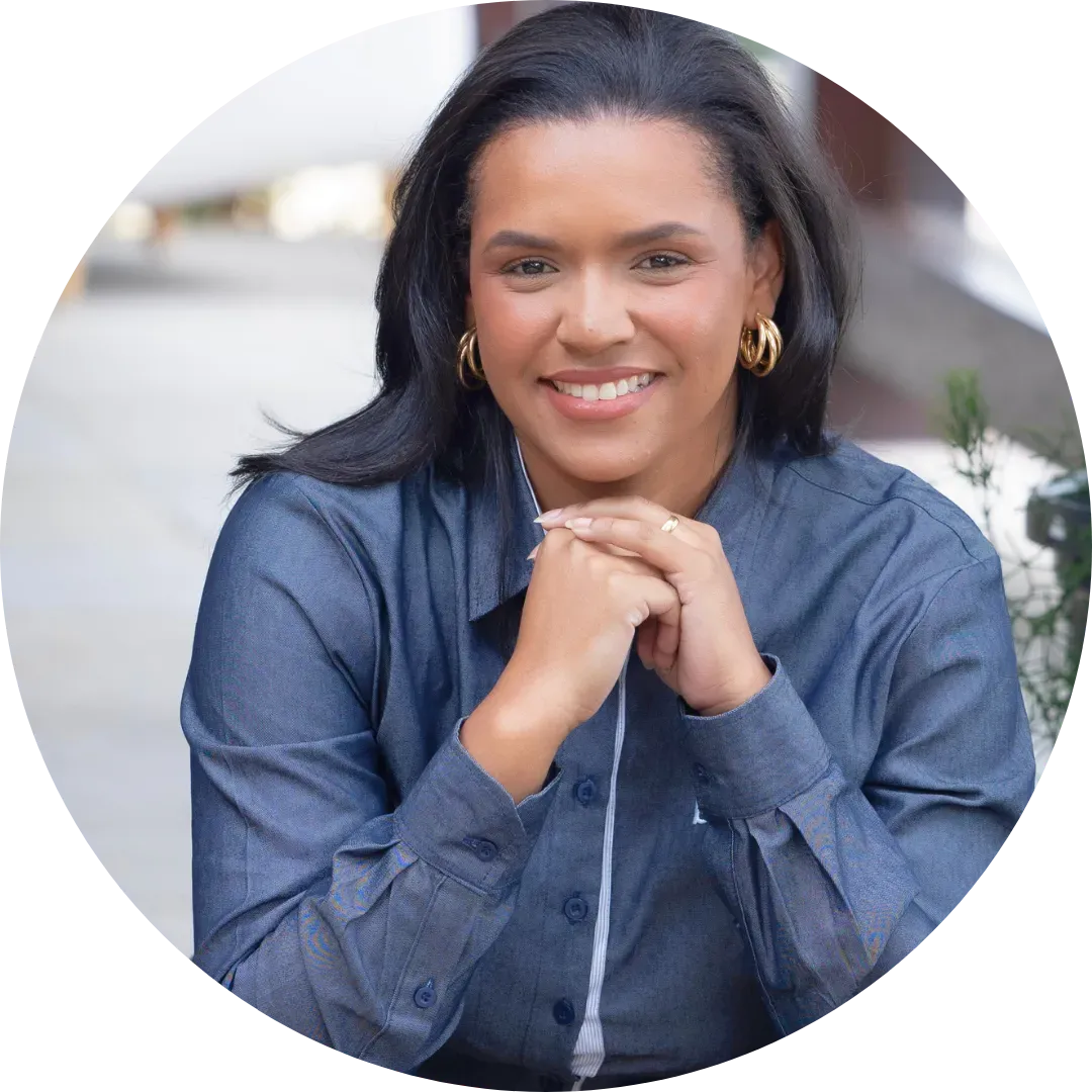 Uma mulher de camisa azul uniforme Bridge Gestão Social está sorrindo com as mãos cruzadas