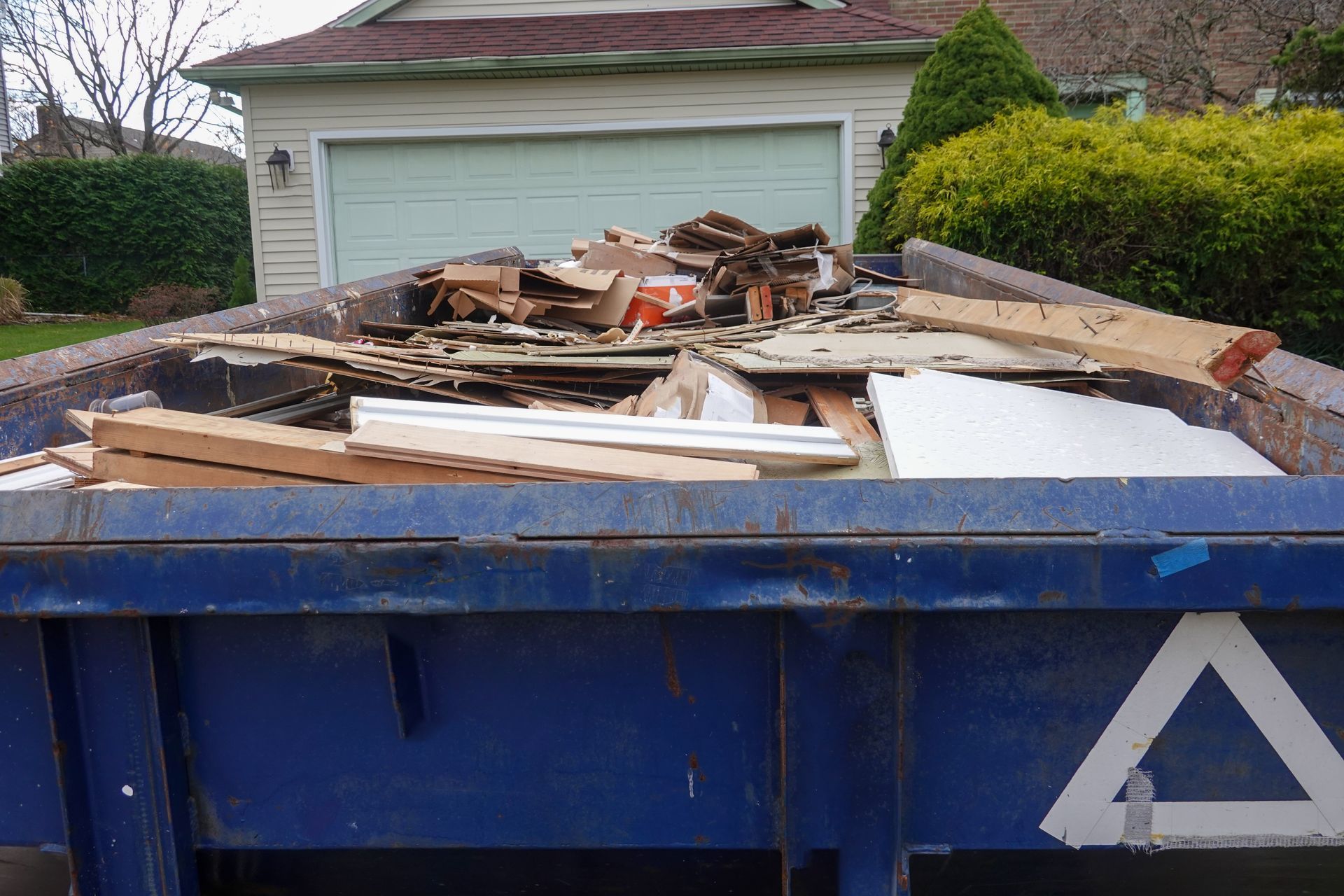 A blue dumpster with a white triangle on the side is full of wood.