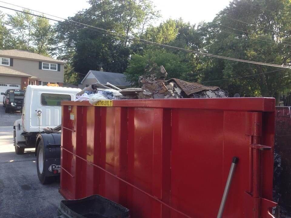 A red dumpster with a white truck in the background