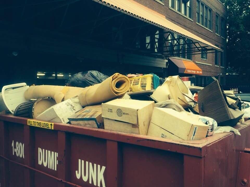 A red dumpster filled with junk in front of a building