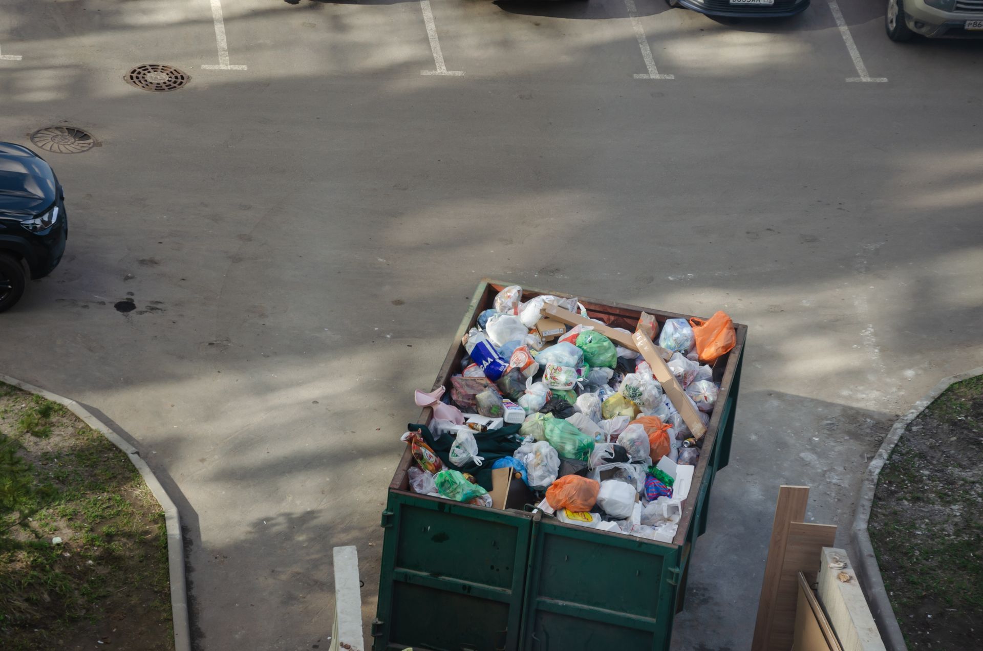 A green dumpster filled with trash is parked in a parking lot.