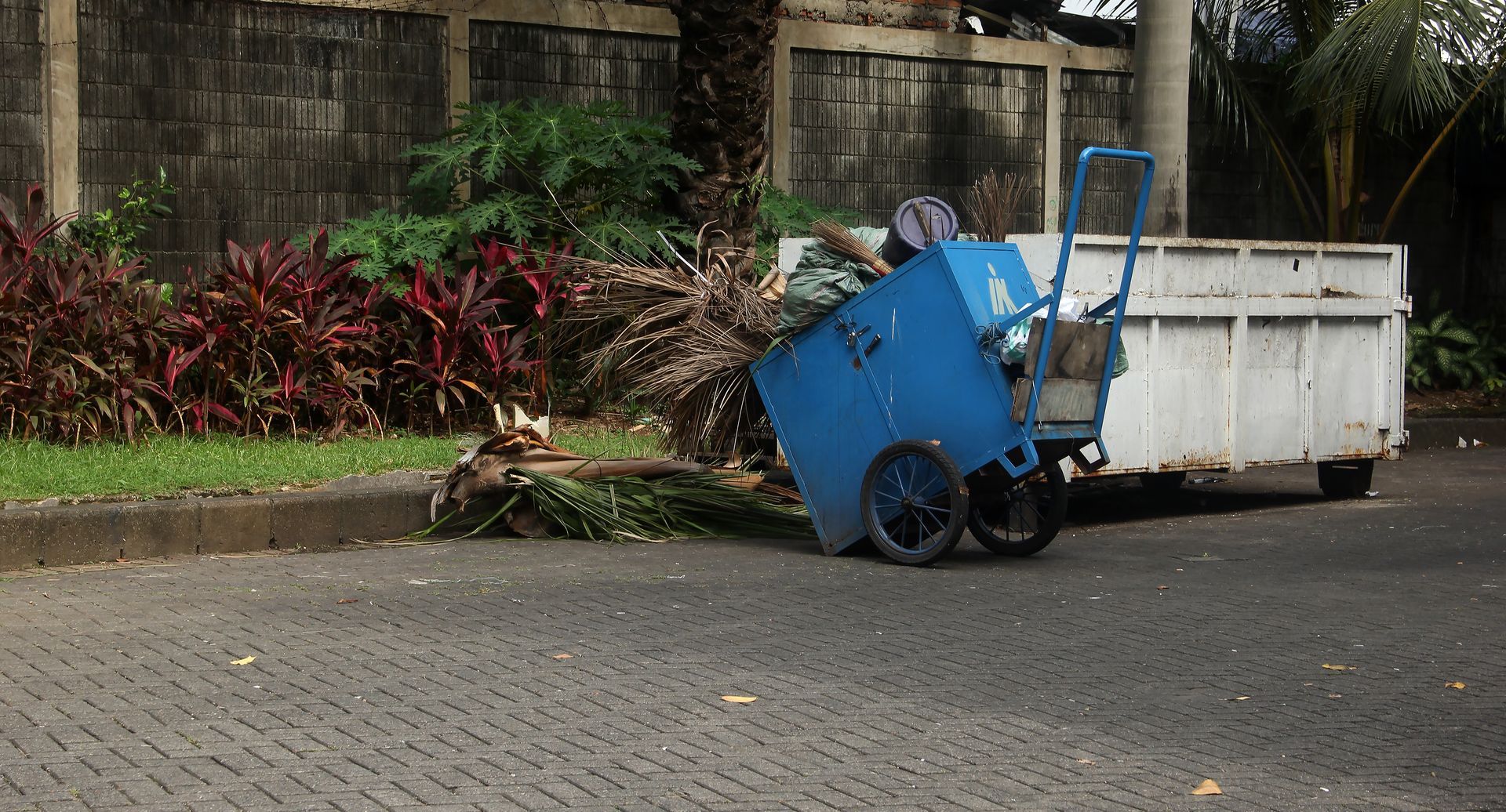 A blue trash can is sitting on the side of the road next to a white truck.