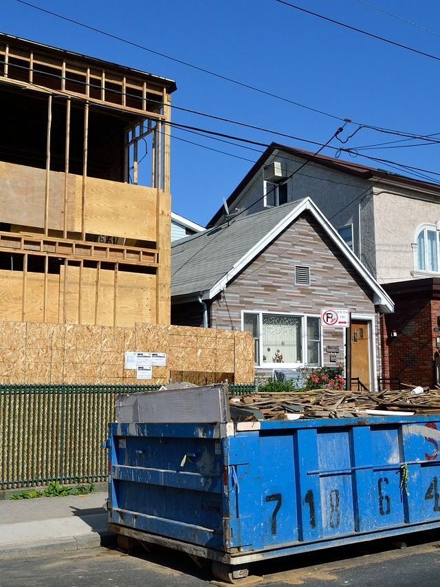 A blue dumpster is parked in front of a house under construction