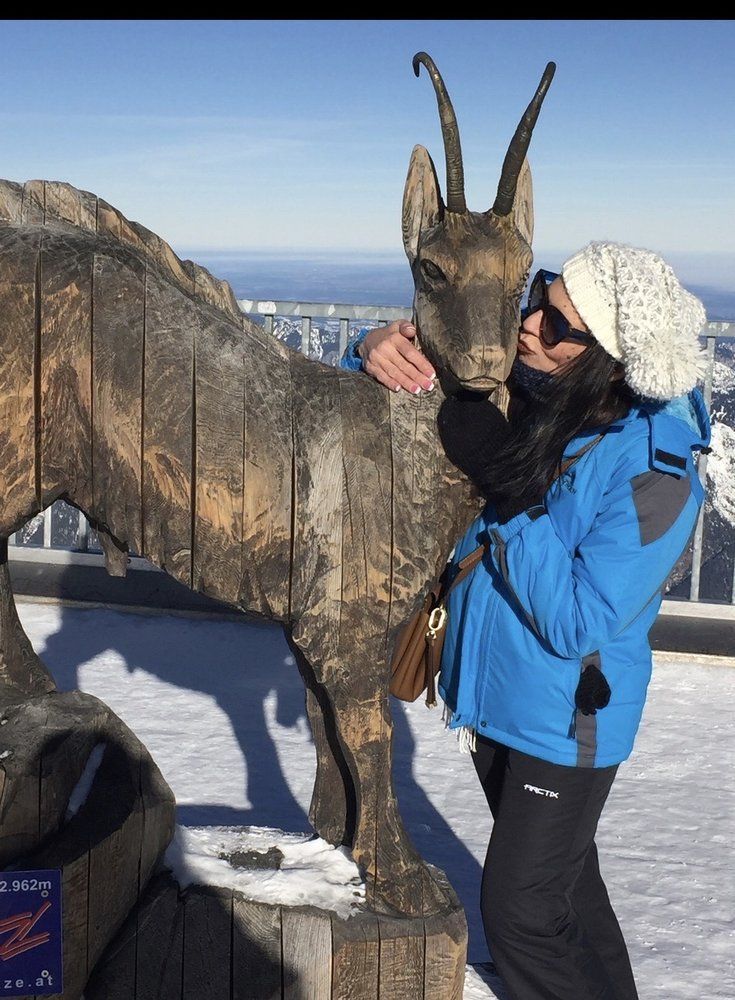 A woman in a blue jacket is standing next to a statue of a goat