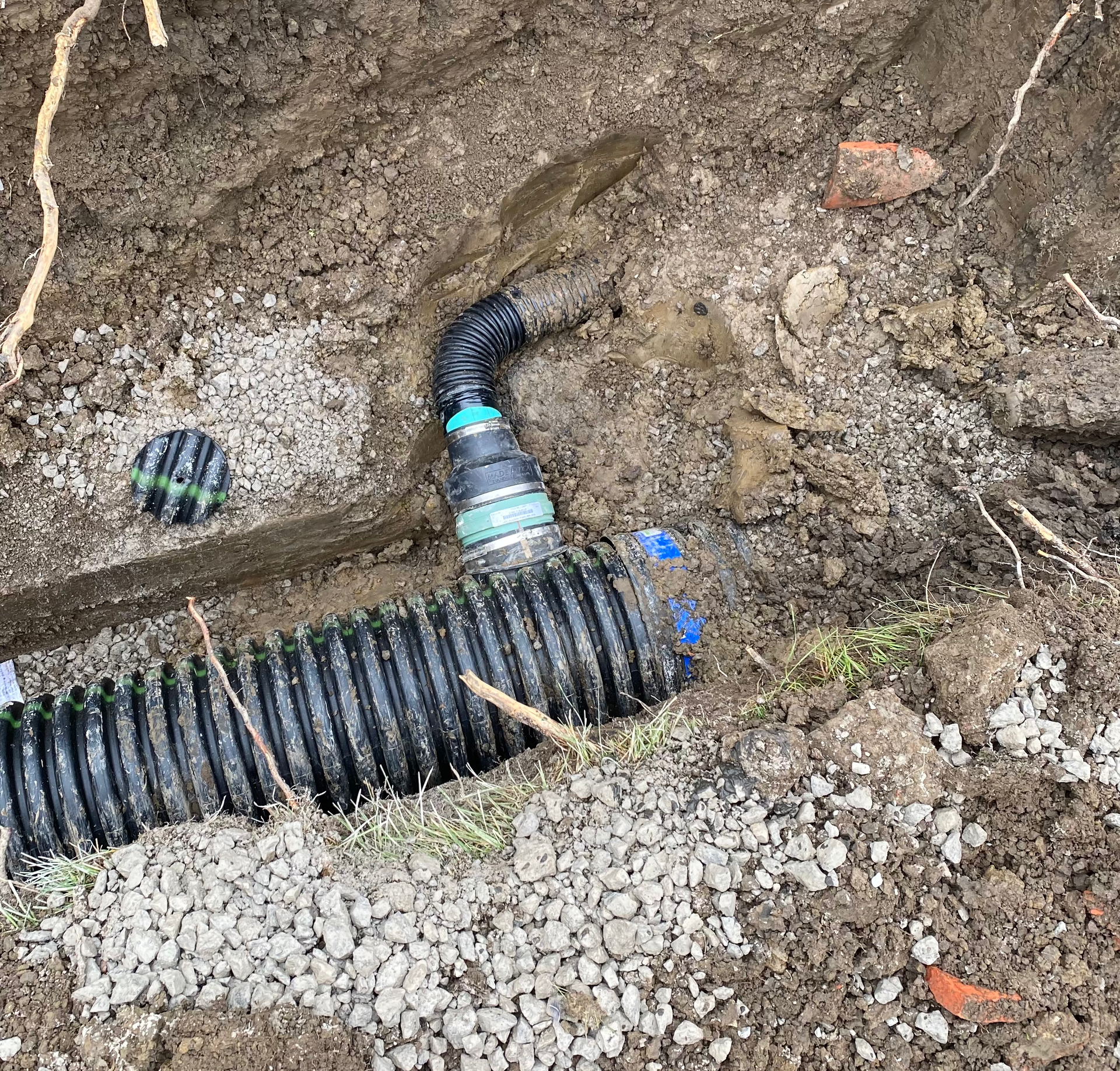 A black pipe is laying in the dirt next to a rock.
