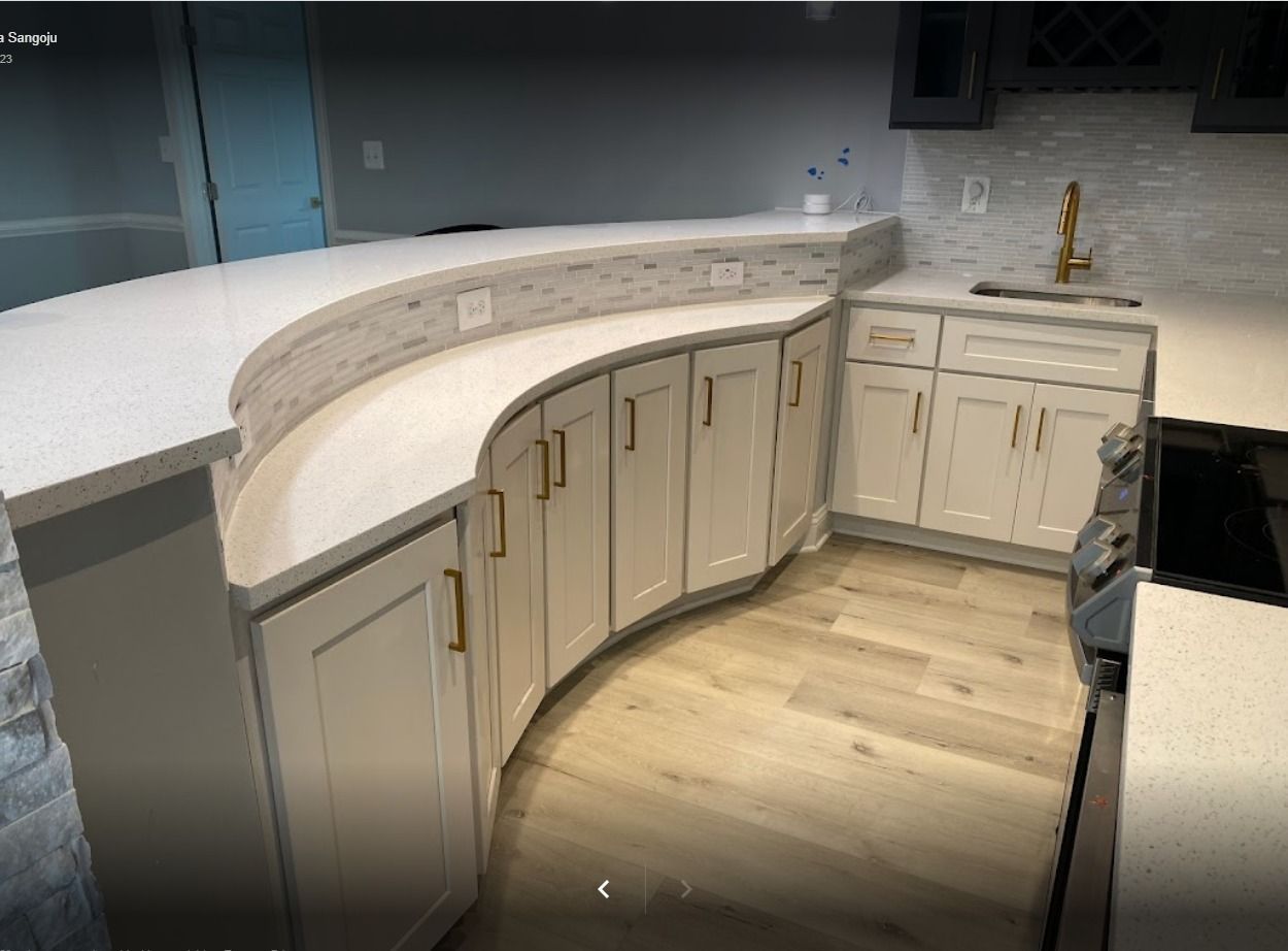 A curved kitchen island with light cabinets and countertop, golden hardware, and wooden floors.
