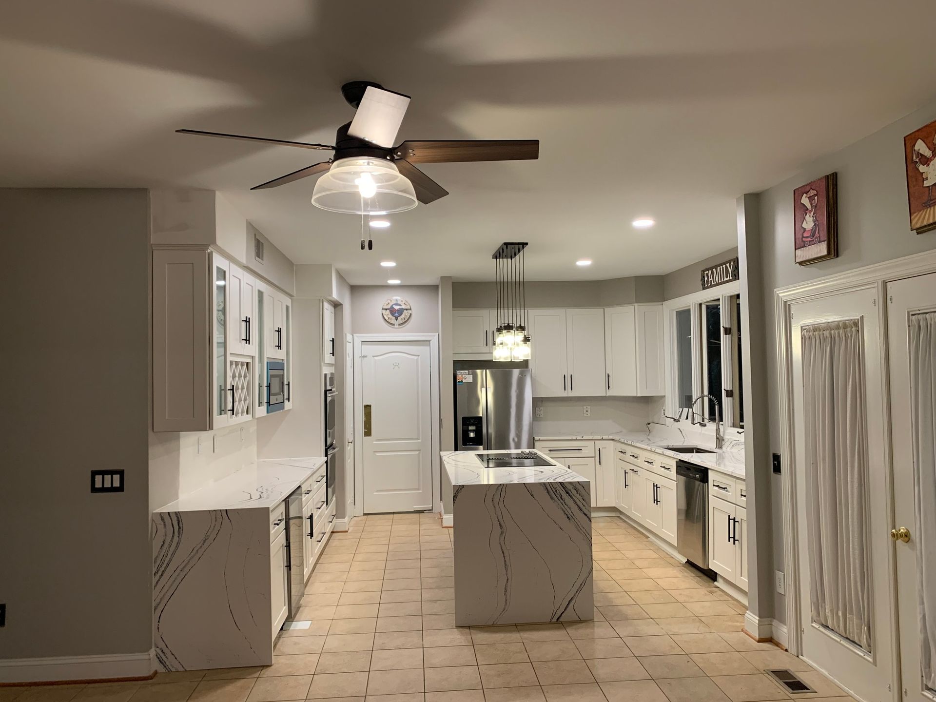 White kitchen with a marble countertop island and matching countertops along the walls. A ceiling fan and rece