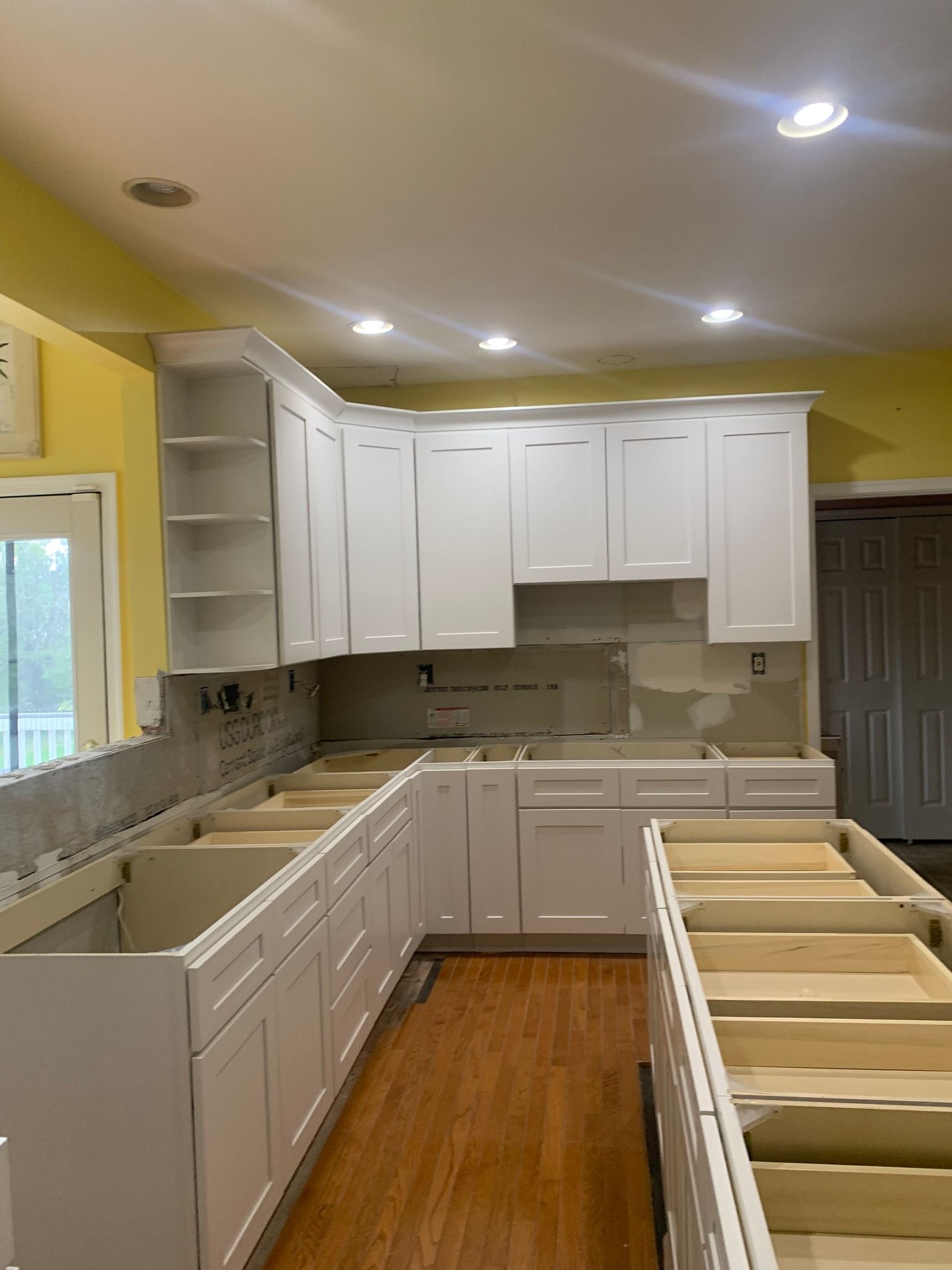 White kitchen cabinets being installed, with open drawers, a wood floor, and yellow walls.