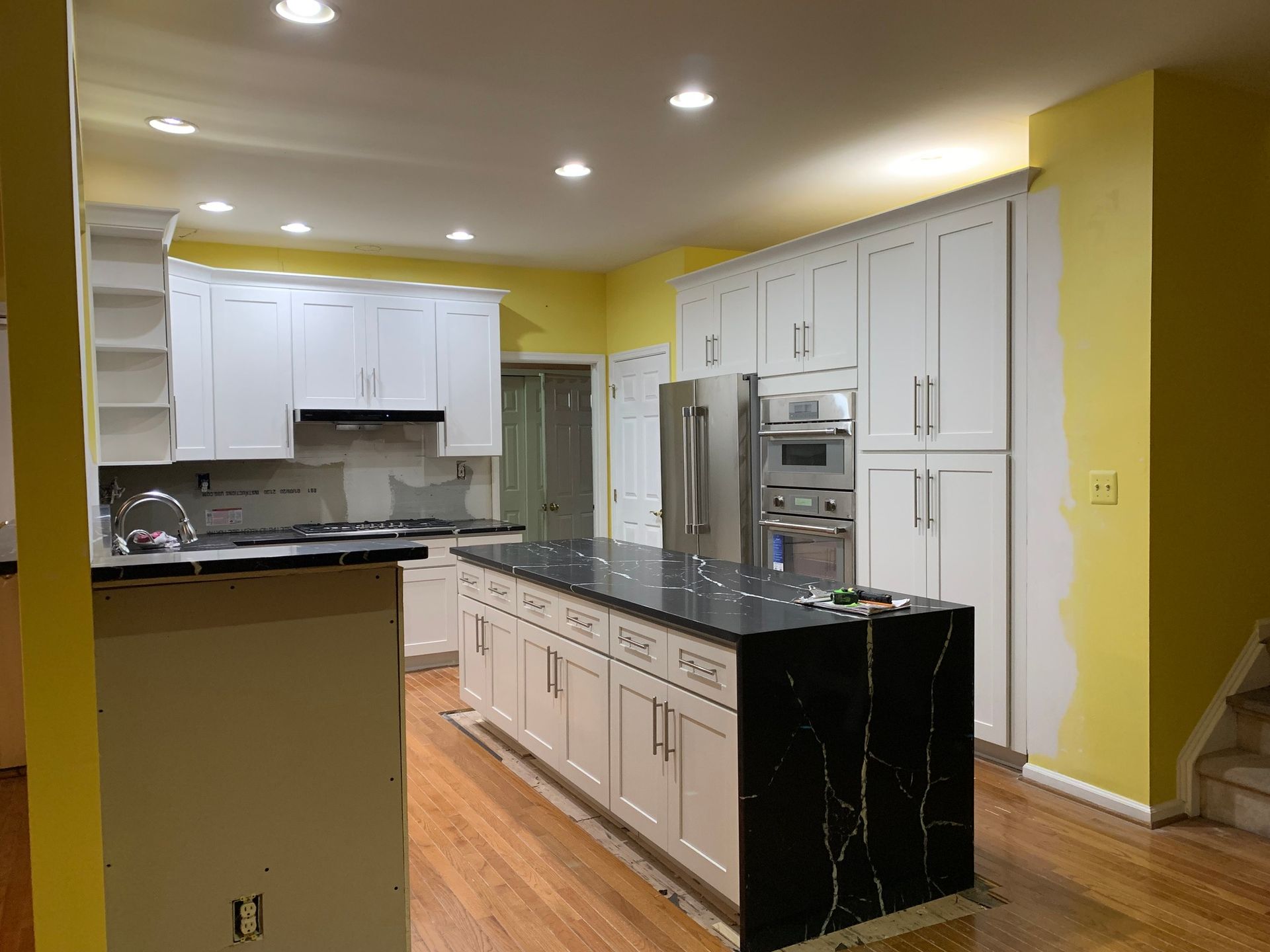 Newly remodeled kitchen with white cabinets, a black countertop island, and yellow walls. Stainless steel appliances.