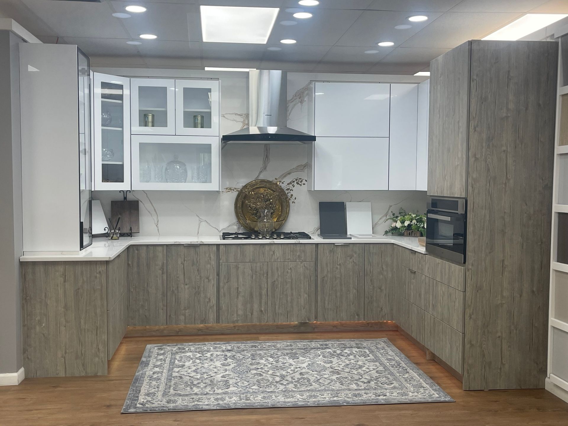 Modern kitchen with white and wood-grain cabinets. A rug lies on the wooden floor.