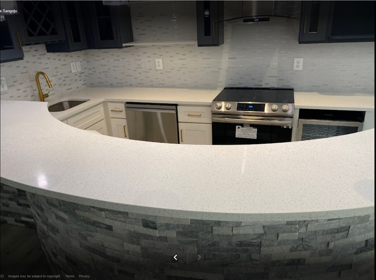 A modern kitchen with a curved white countertop, stainless steel appliances, and a gray stone-like base.