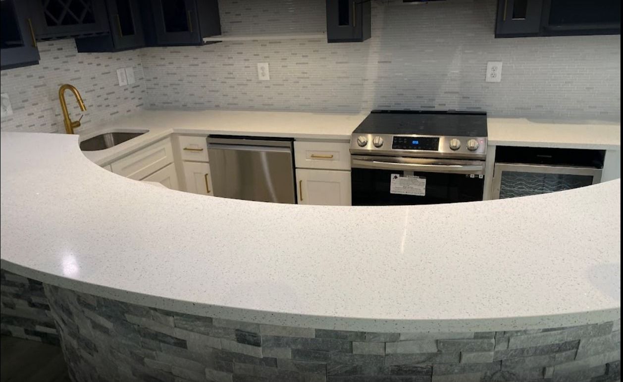 A kitchen with a white countertop that curves around the sink and stove, with gray brick-like facade below.