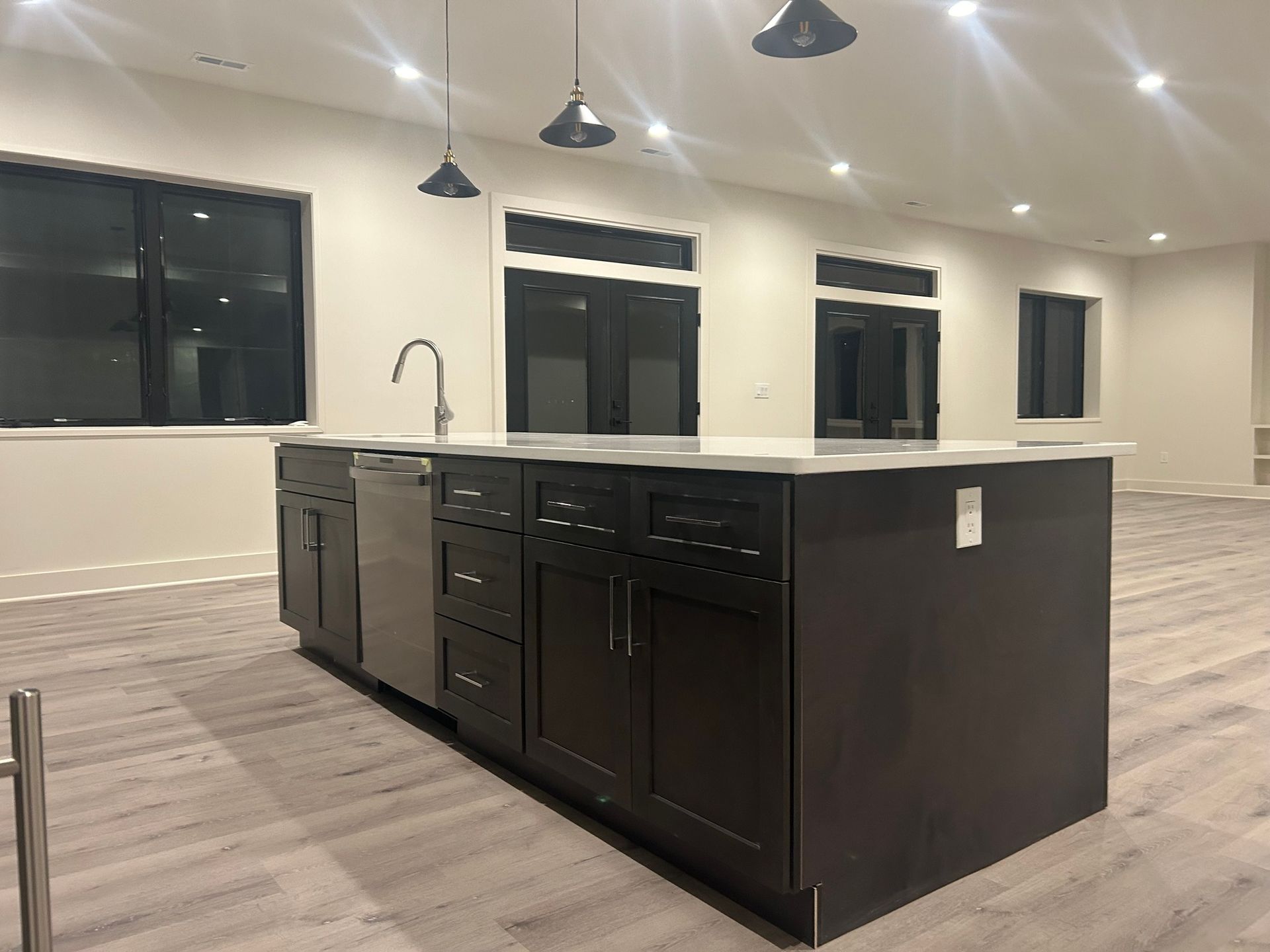 Dark brown kitchen island with sink and dishwasher. Light flooring and walls.