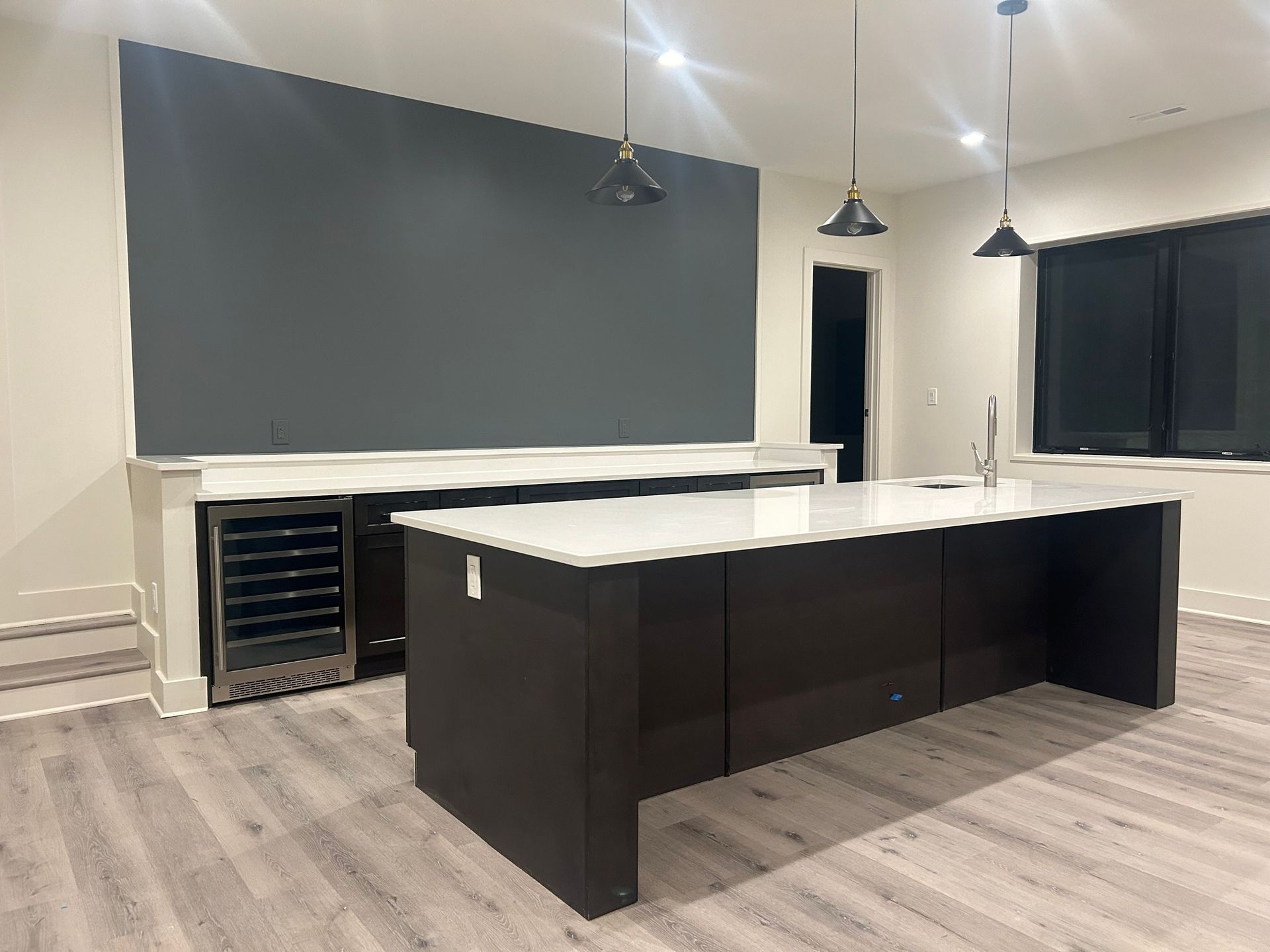 Modern kitchen with a dark island and a gray accent wall. A built-in wine fridge is visible near the wall.