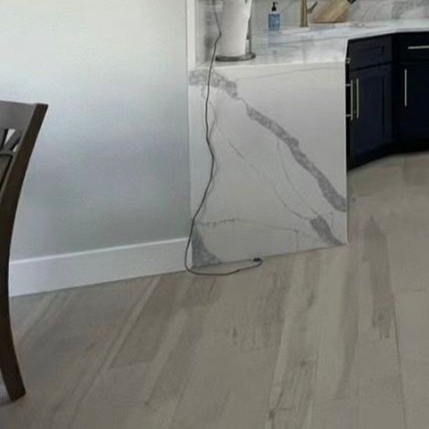 Light wood-look flooring and a section of a white and gray marble-look kitchen cabinet. A chair is visible on the left.