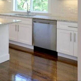 Stainless steel dishwasher in a white kitchen with granite countertops and dark wood floors.