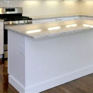 White kitchen island with a granite countertop in front of a gas range. The 
