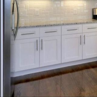 White kitchen cabinets with silver hardware and a granite countertop, beneath a white subway tile backsplash.