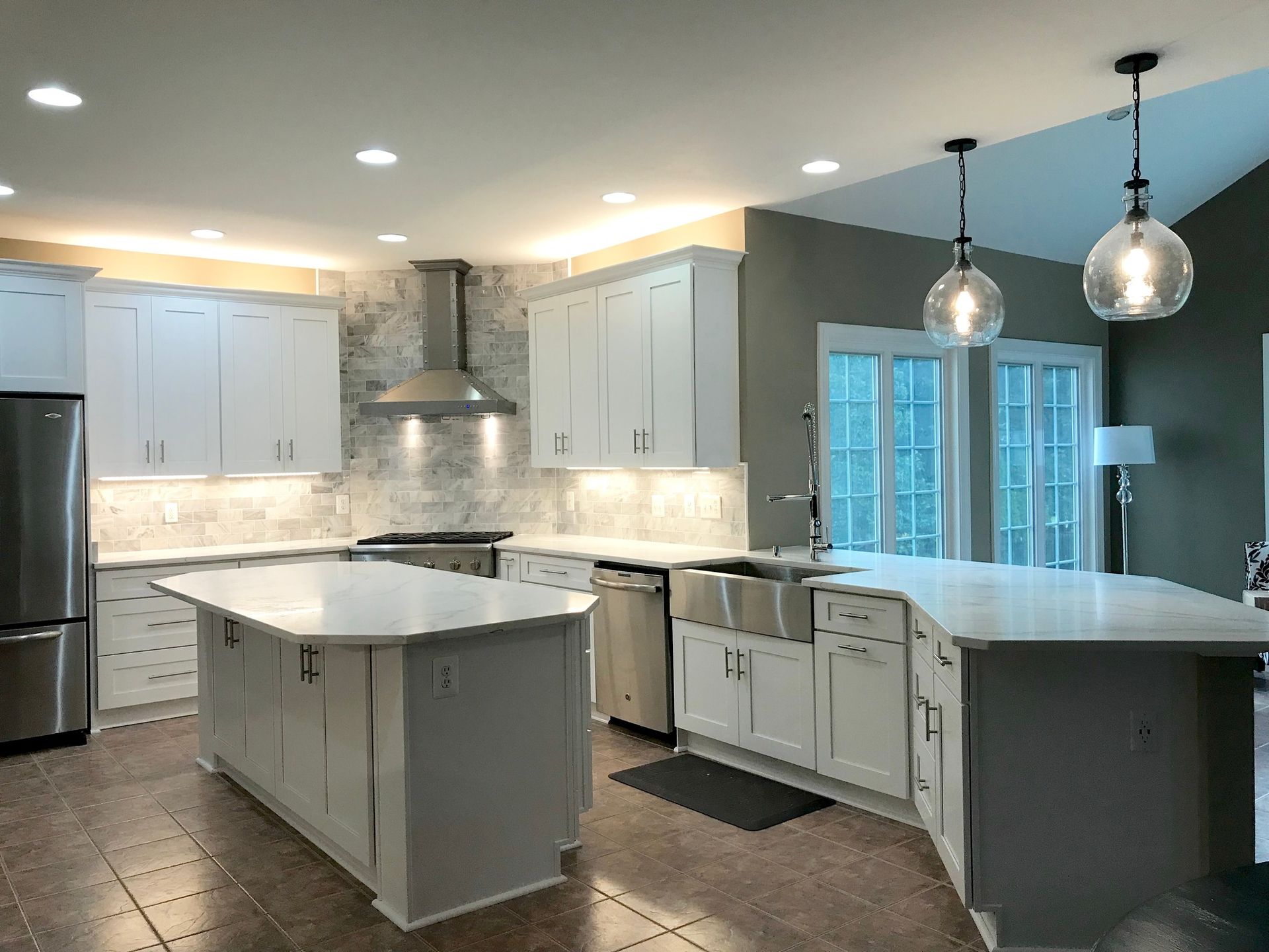 Modern kitchen with white cabinets, light countertops, and two islands. Stainless steel appliances and globe pendant lights.