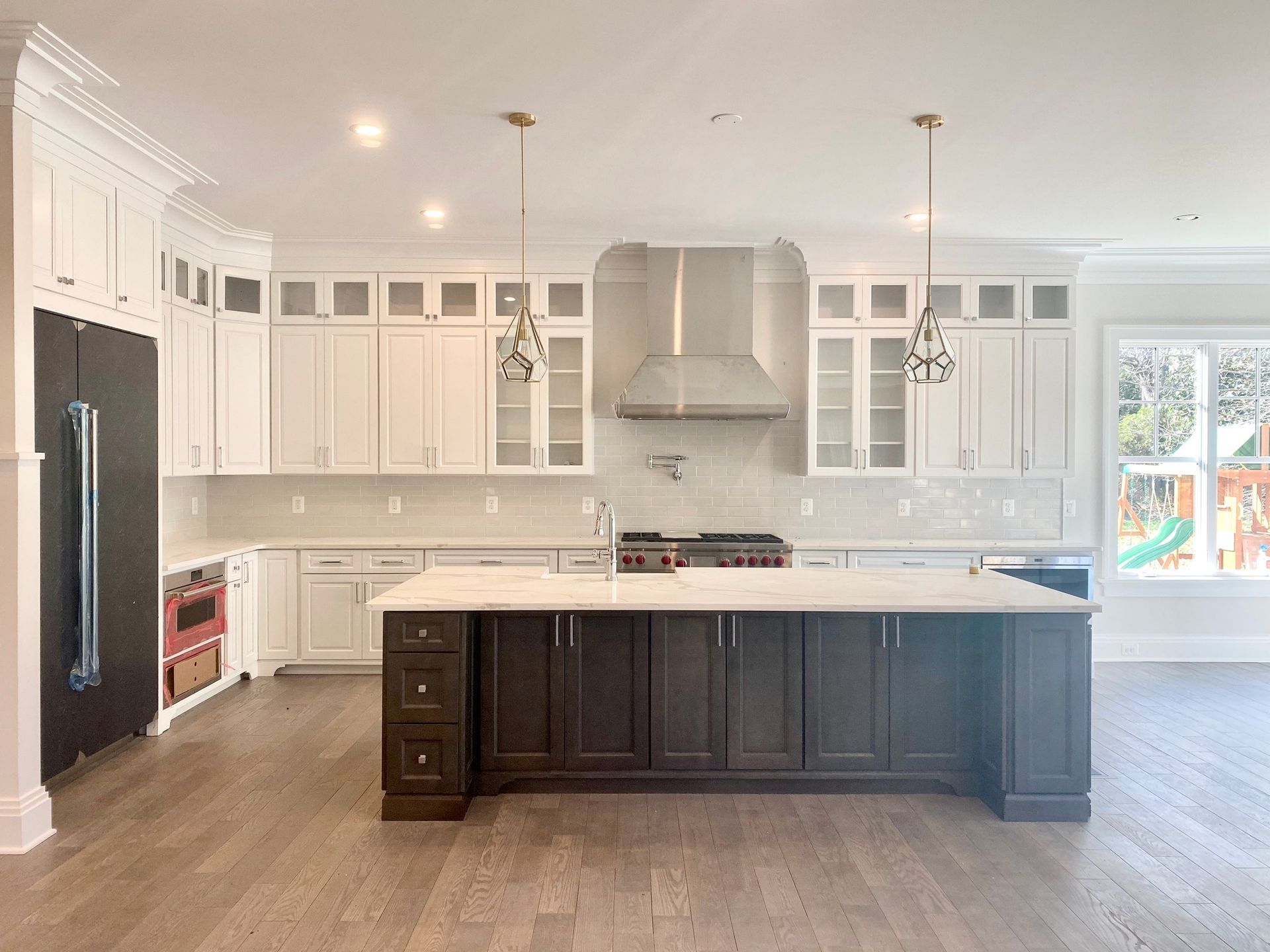 Spacious kitchen with a dark brown island, white cabinets, and stainless steel appliances. Light hardwo