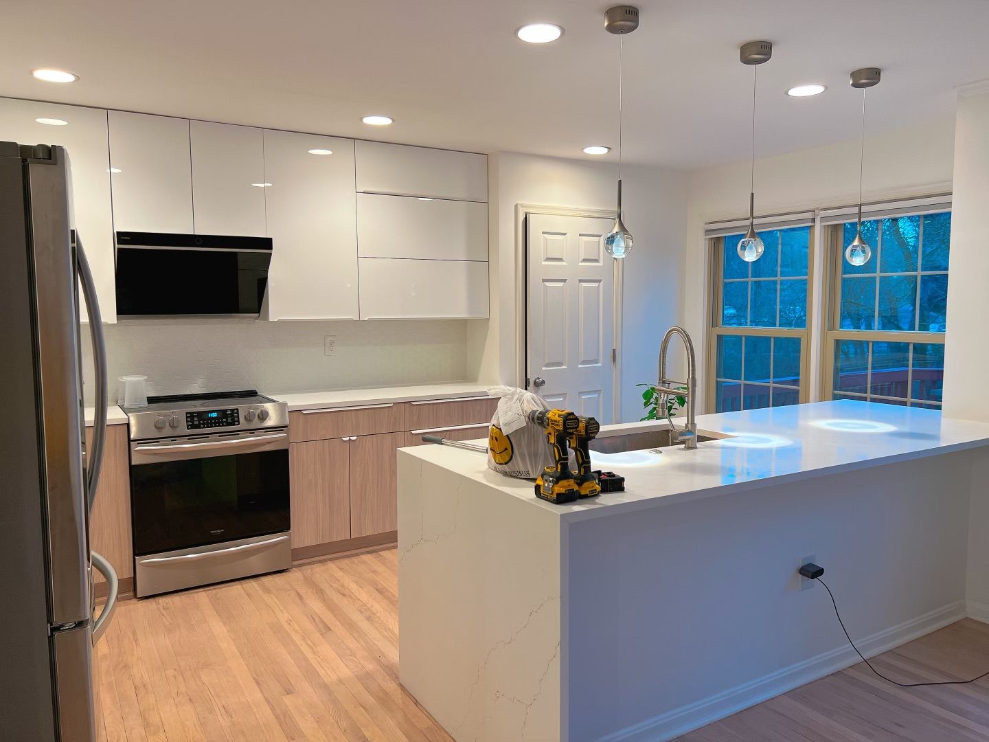 Modern kitchen with white and light wood cabinets, stainless steel appliances, and a white island with a sink.