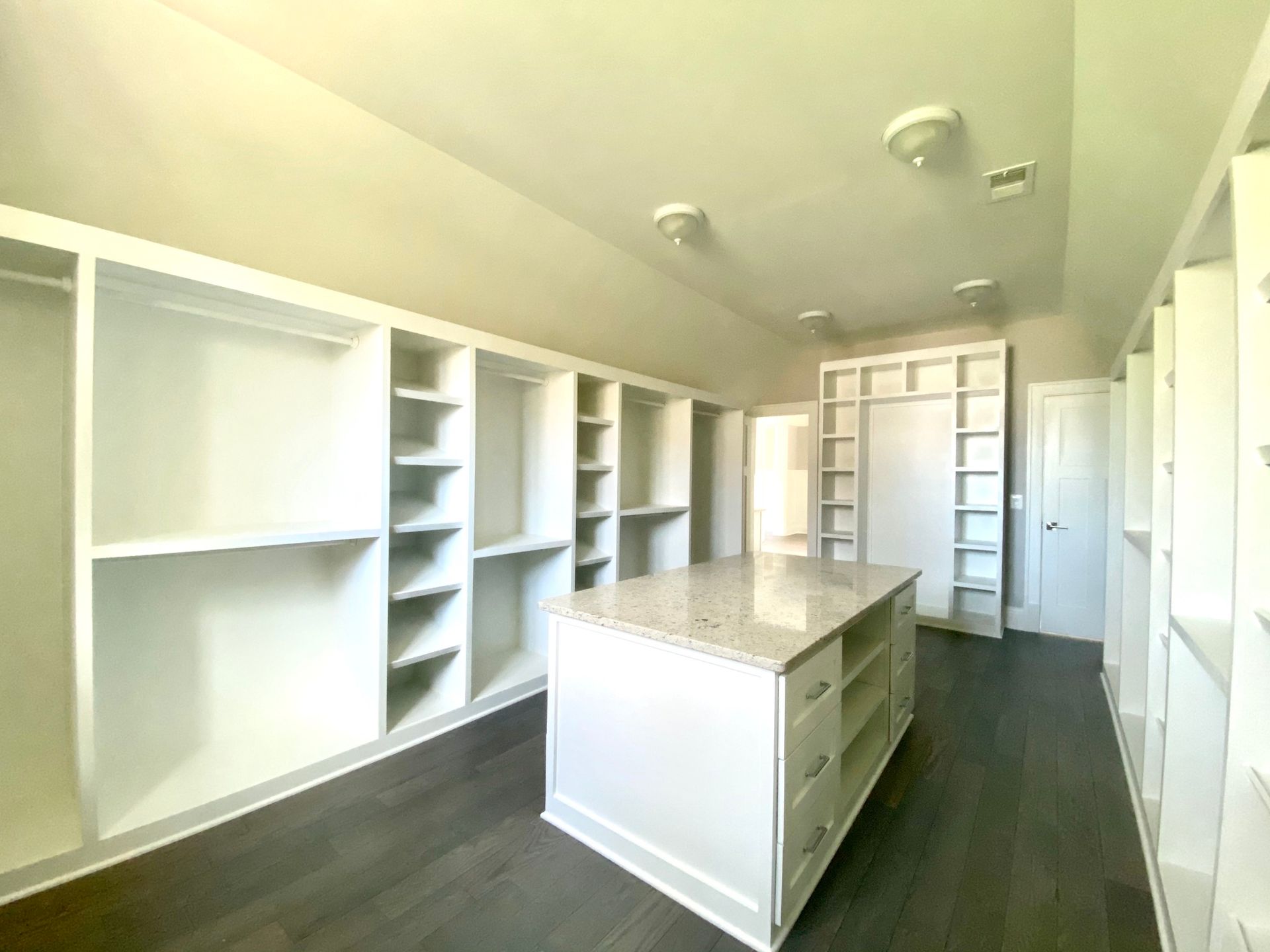 White kitchen with a countertop island, white cabinets, white appliances, and light wood flooring.