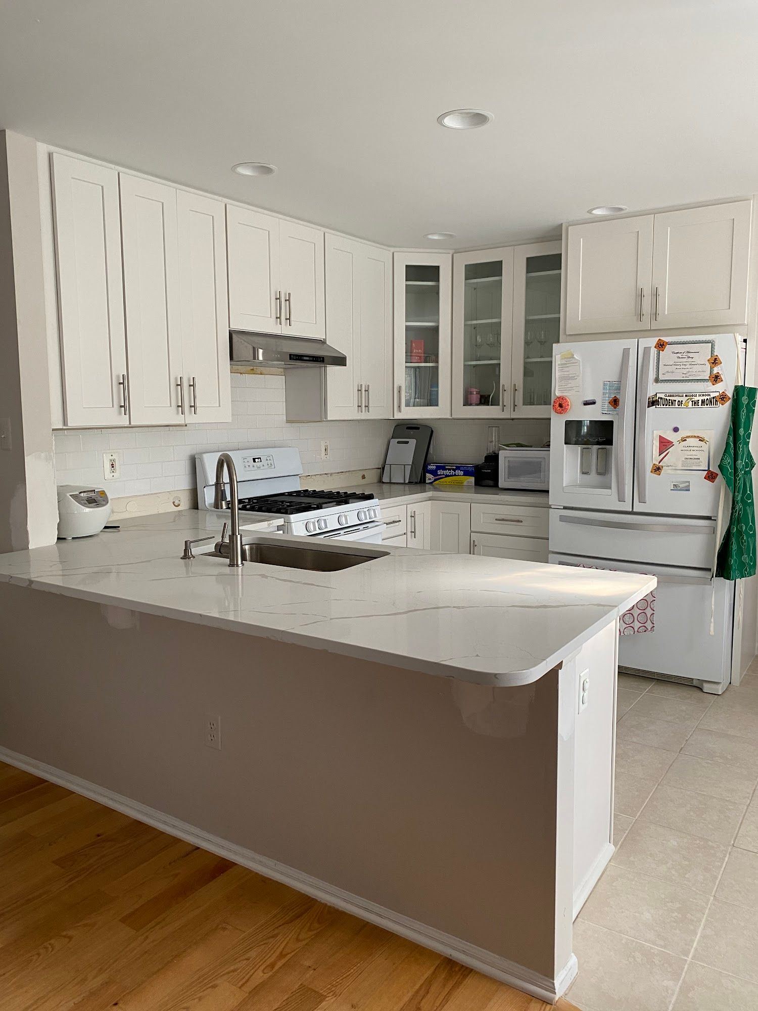White kitchen with a countertop island, white cabinets, white appliances, and light wood flooring.