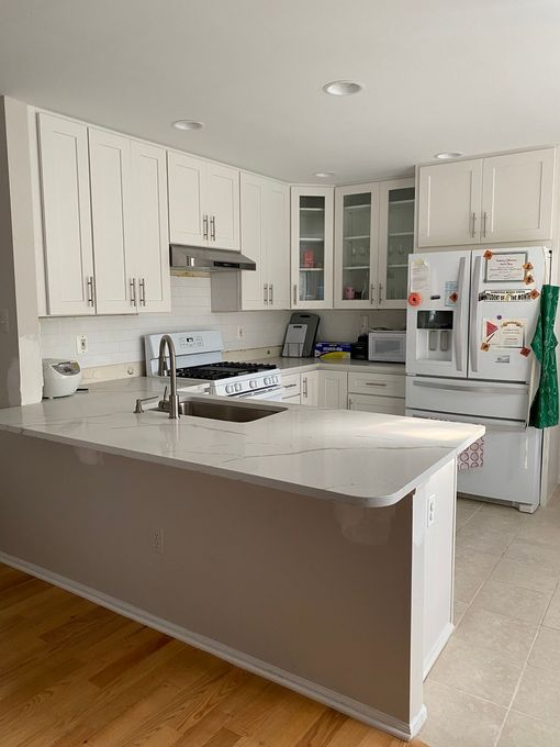 White kitchen with a countertop island, white cabinets, white appliances, and light wood flooring.