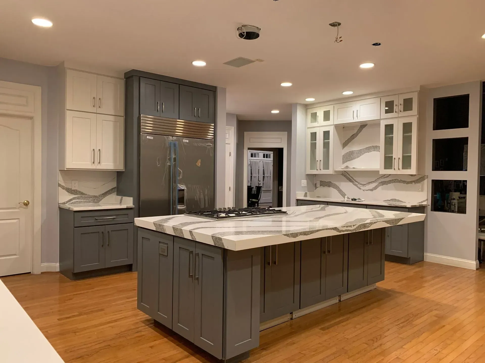 A modern kitchen with gray and white cabinets, a large island with a marble 