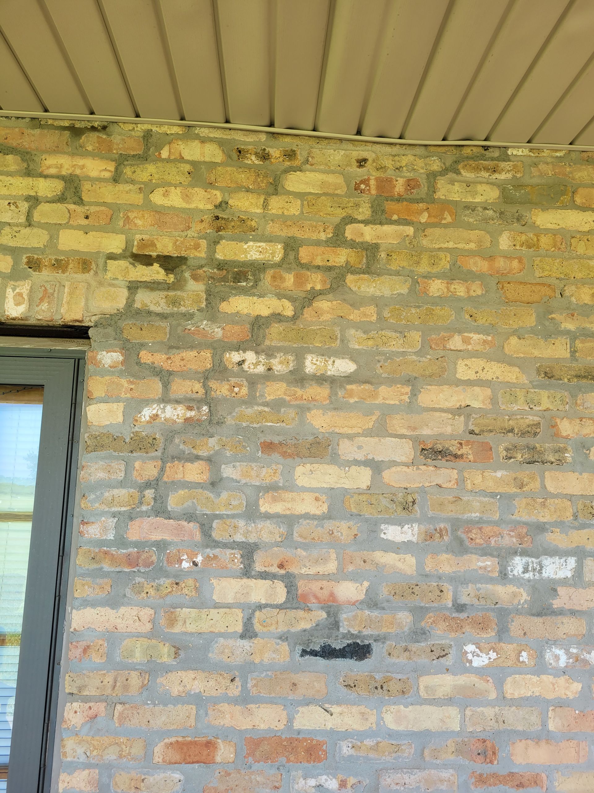 Tan brick wall with green and black discoloration under a beige overhang.