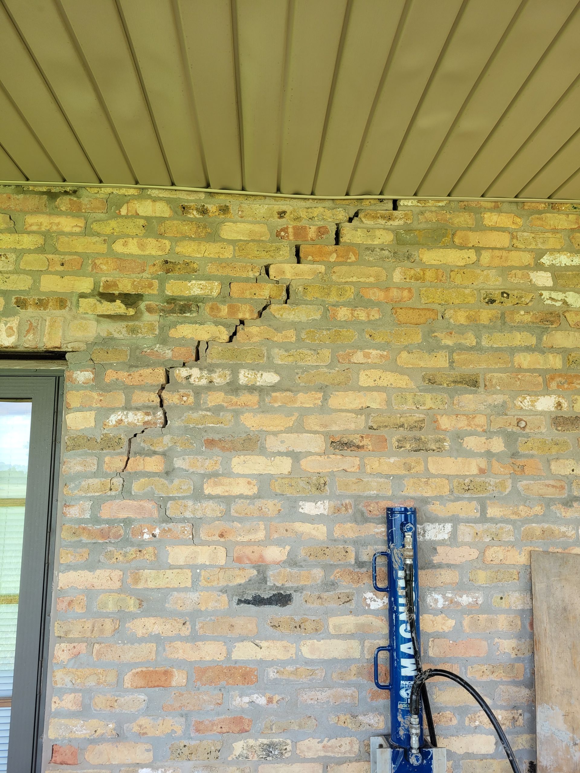 Cracked brick wall with visible cracks. Blue support jack visible.