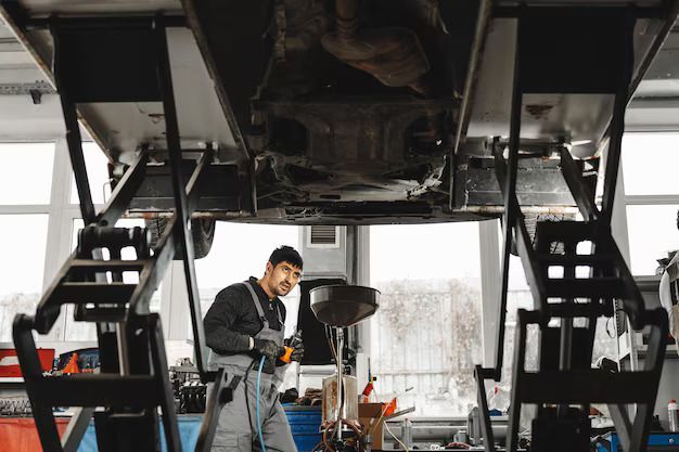 Mechanic under a car on a lift, draining oil into a pan. Workshop setting | Central Florida Diesel Performance