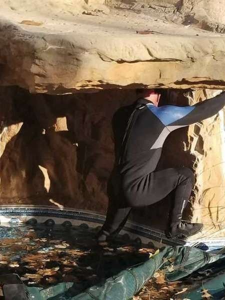 A man in a wet suit is kneeling down in a cave