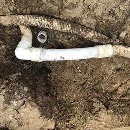 A white pipe is laying in the dirt next to a hose.