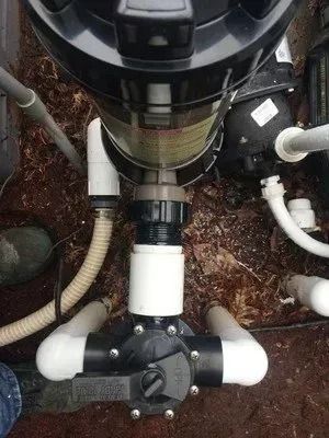 A vacuum cleaner is sitting on top of a swimming pool surrounded by pipes.