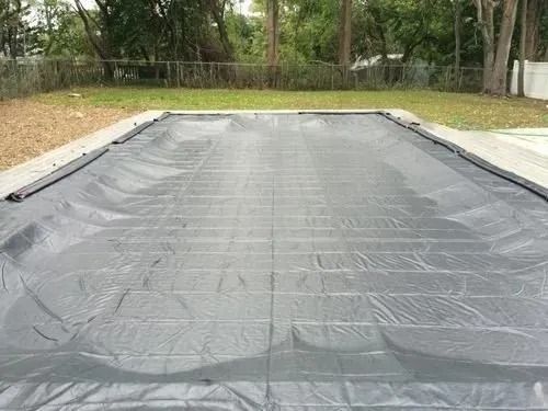 A black pool cover is sitting on top of a swimming pool.