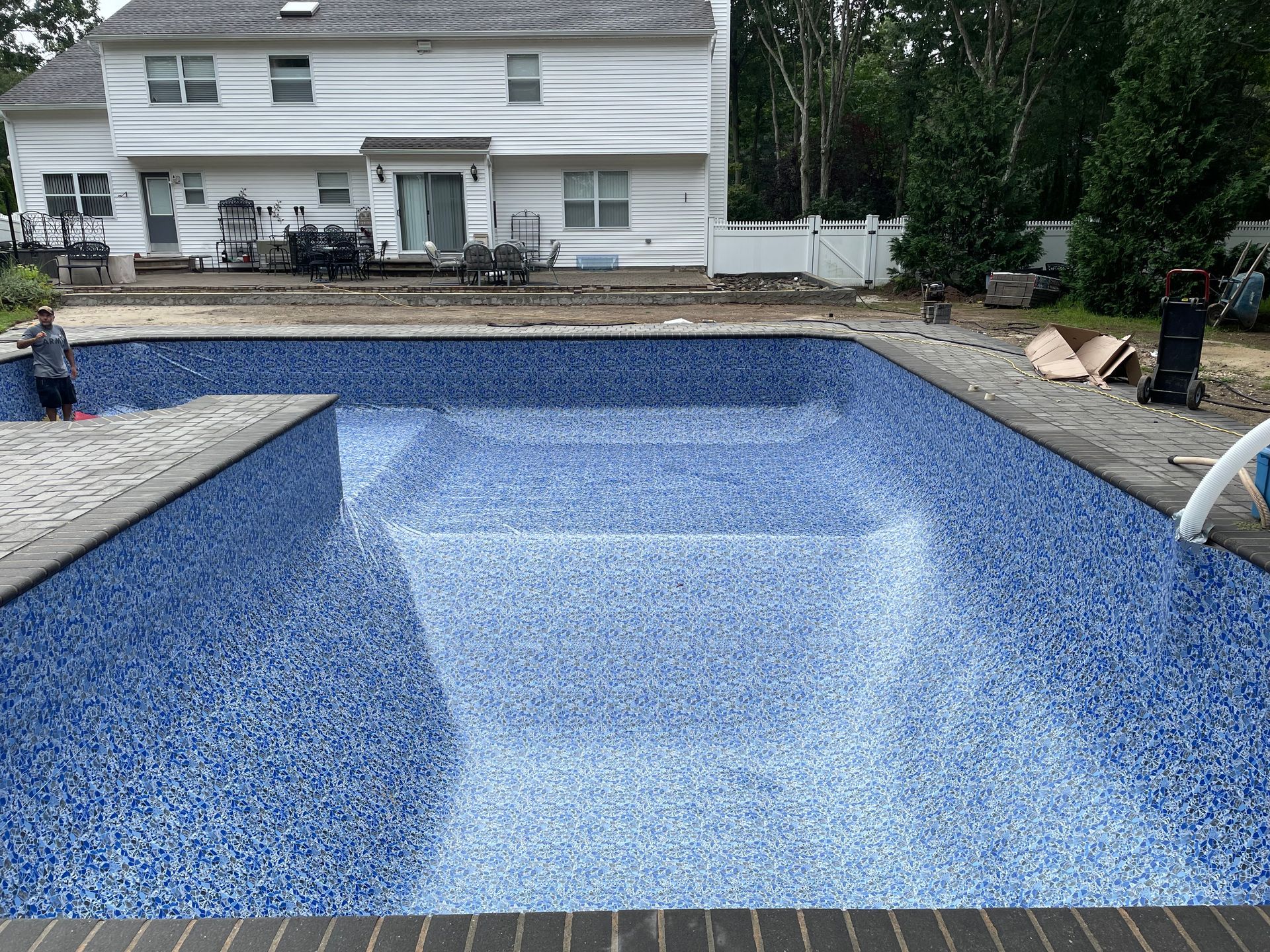 A man is laying tiles on the floor of a swimming pool.