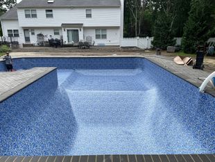 A large swimming pool with chairs around it and a staircase leading to it.