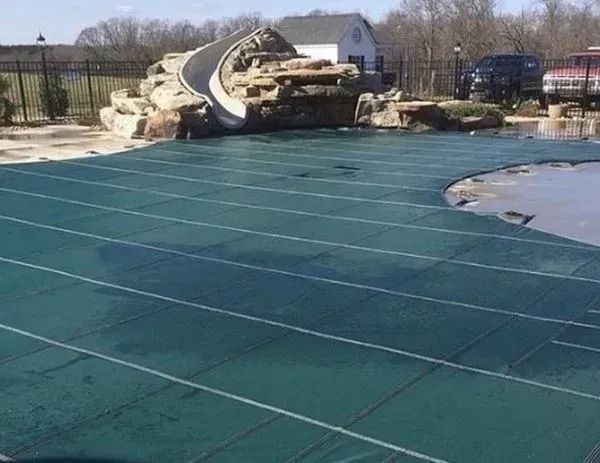 A swimming pool with a slide and a green cover on it.