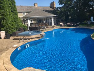 A large swimming pool with chairs around it and a staircase leading to it.