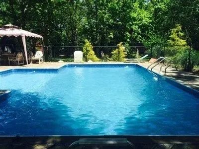 A large swimming pool surrounded by trees and a gazebo.