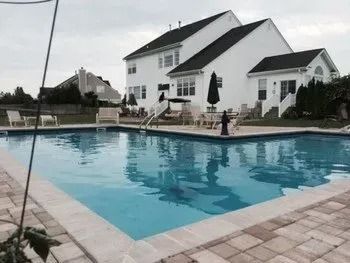 A large swimming pool in front of a white house.