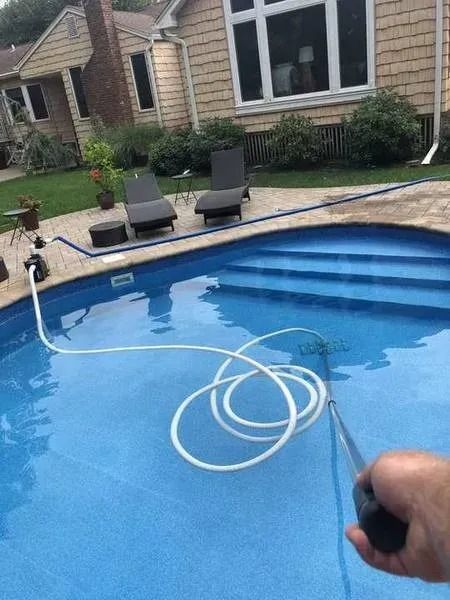 A person is holding a hose in front of a swimming pool.