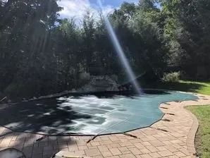 The sun is shining through the trees over a swimming pool.