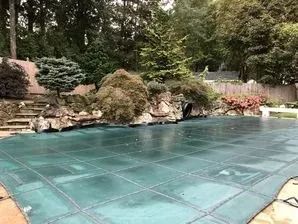 A swimming pool with a green cover on it and trees in the background.