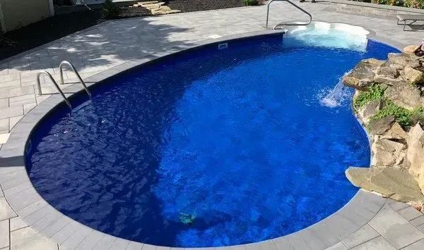 A small oval swimming pool with a waterfall in the middle of it.