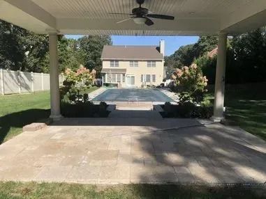 A patio with a ceiling fan and a large house in the background.