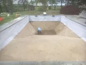 A man is standing in the middle of a swimming pool filled with sand.